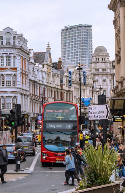 A busy street scene in an urban area near Hyde Park, with a red double-decker bus displaying route number 14 and destination Putney Heath in the foreground. The bus is approaching a pedestrian crossin